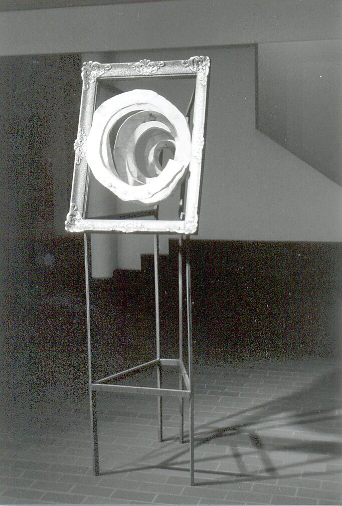 ‘Houten spiralen en metalen’: Metalen kader met houten spiraalvormen in decoratieve lijst op hoge metalen standaard; zwart-wit tentoonstelling, CC Leopoldsburg, 1999.