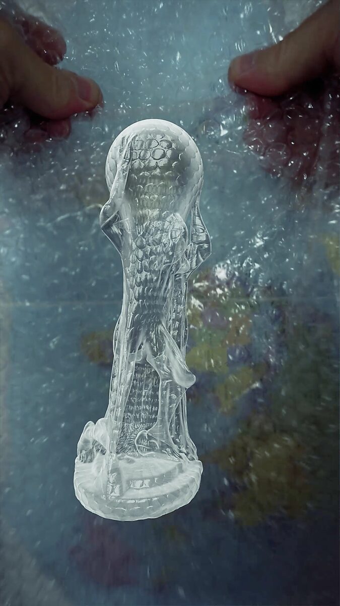 Virtuele transformatie — Atlas in bubbelplastic: videostill uit een 3D-animatie; de Atlasfiguur strekt zich uit en wordt langgerekt, terwijl de textuur van het bubbelplastic zich als een huid over het lichaam en de bol lijkt te verspreiden.
