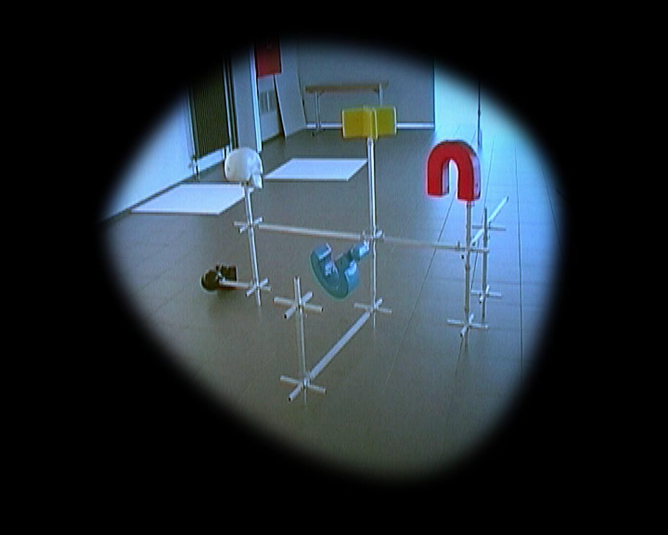 Choose and Change, Moving Installation — video still: construction with scattered colored forms and a red U-shape, viewed from an elevated perspective within a circular cut-out.