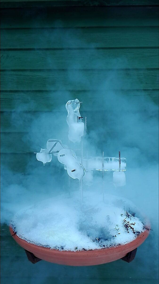 Entropische sculptuur nr. 1 — videostill van het sculptuur in de winter met bevroren ijsvormen en opstijgende damp boven de met sneeuw bedekte schaal.