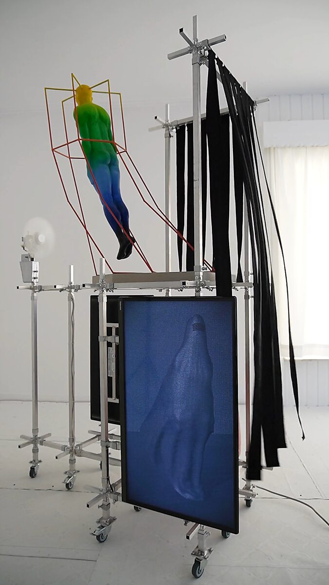Thermal Promise — video still featuring the projection of a woman in a burqa while the fan sets the fabric strips in motion, allowing image, body and wind to form a performative space.