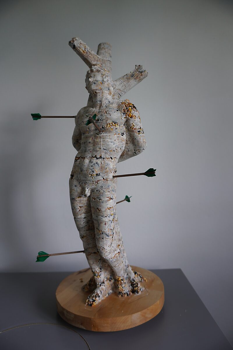 St. Sebastian with Birds No. 2 — process photo of a test cast of the figure in fat and birdseed, pierced with arrows and placed on a round wooden base.