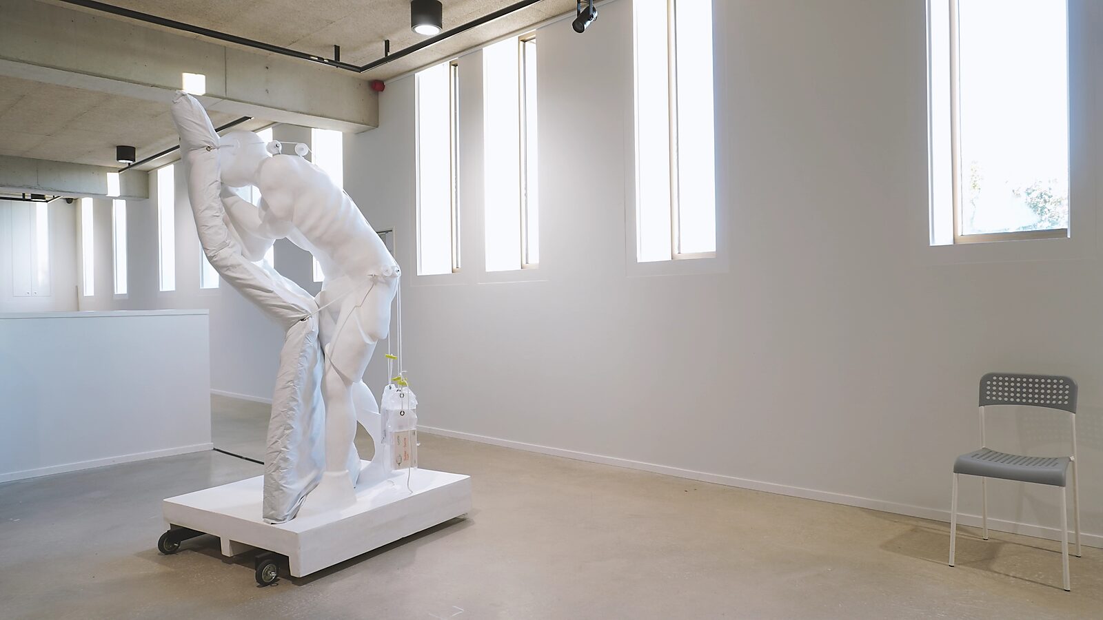 Uitslapen met de slapers — videostill van het kunstwerk op de tentoonstelling Transformatiestudio nr.1: warm of koud, CC De Adelberg Lommel: het luchtmatras staat opnieuw volledig rechtop terwijl het beeld ertegen gebogen blijft staan.
