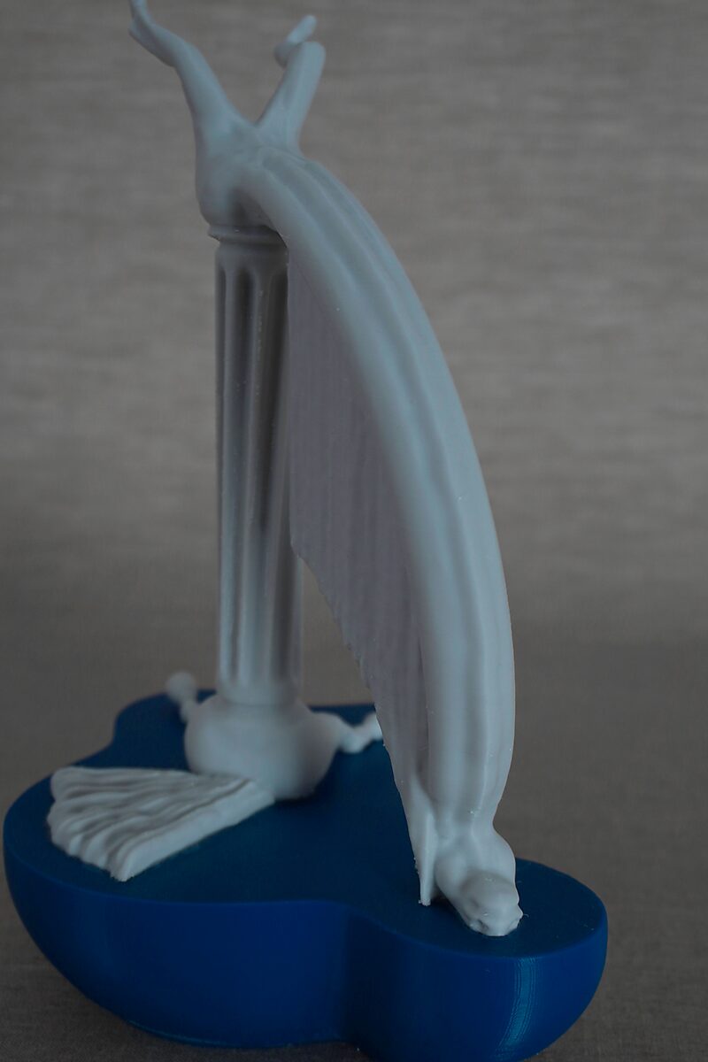 The Columns of Ovid, Ocyrhoë — detail view of a white 3D-printed wing-like form bending downward from a column and ending on a blue sculptural platform.
