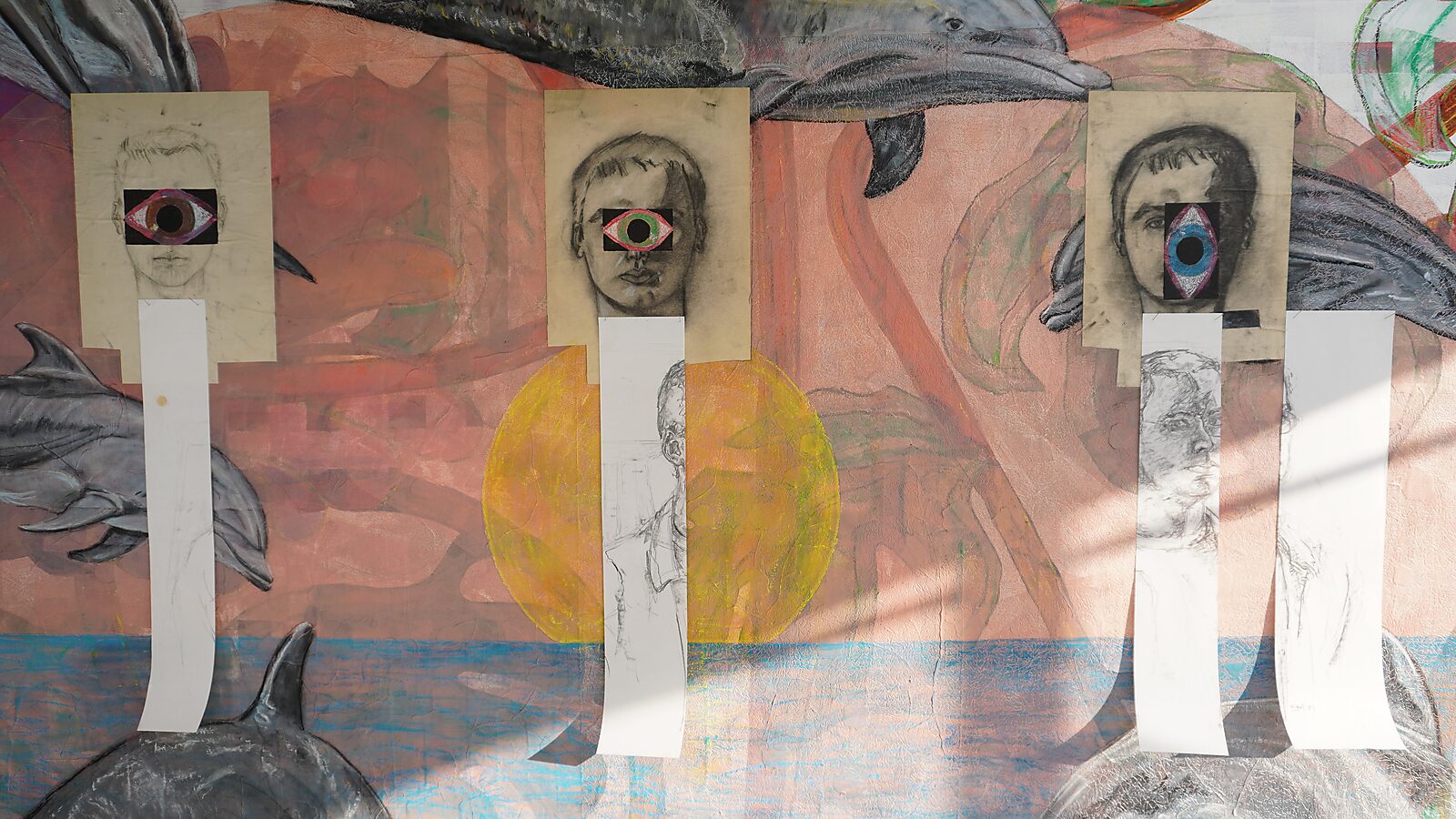 Naming–Value Butterflies — process drawing: self-portrait study (1995), Captured (2026) — three self-portraits hang side by side, each with an eye-shaped cut-out and long paper strips below.
