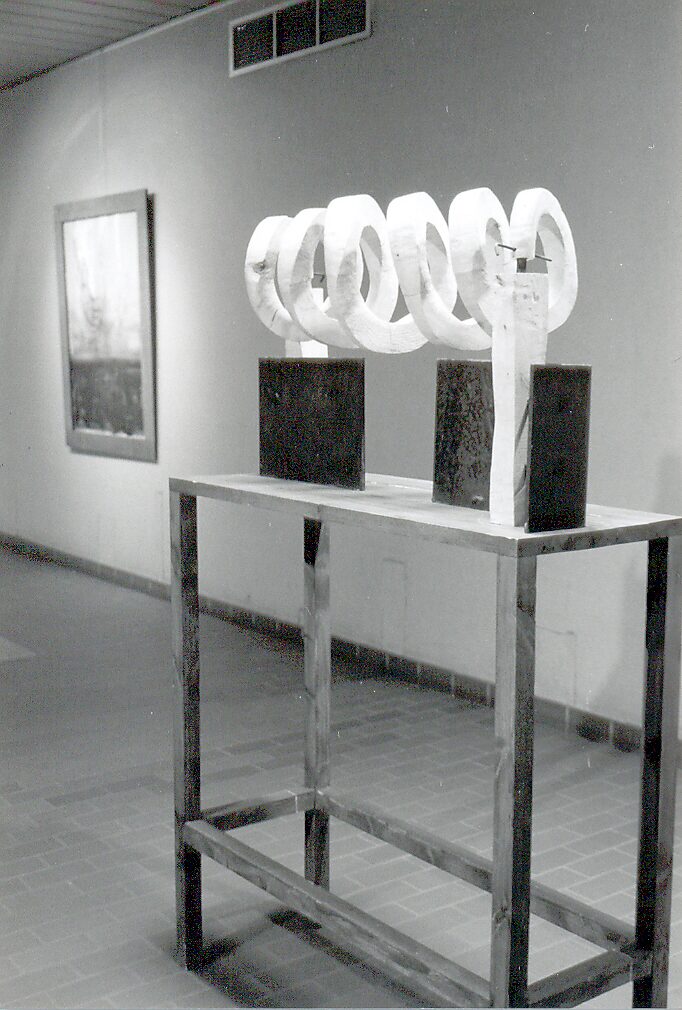 ‘Houten spiralen en metalen’: Wooden spirals mounted on metal supports on a table structure; combination of wood and metal, black-and-white exhibition view, CC Leopoldsburg, 1999.