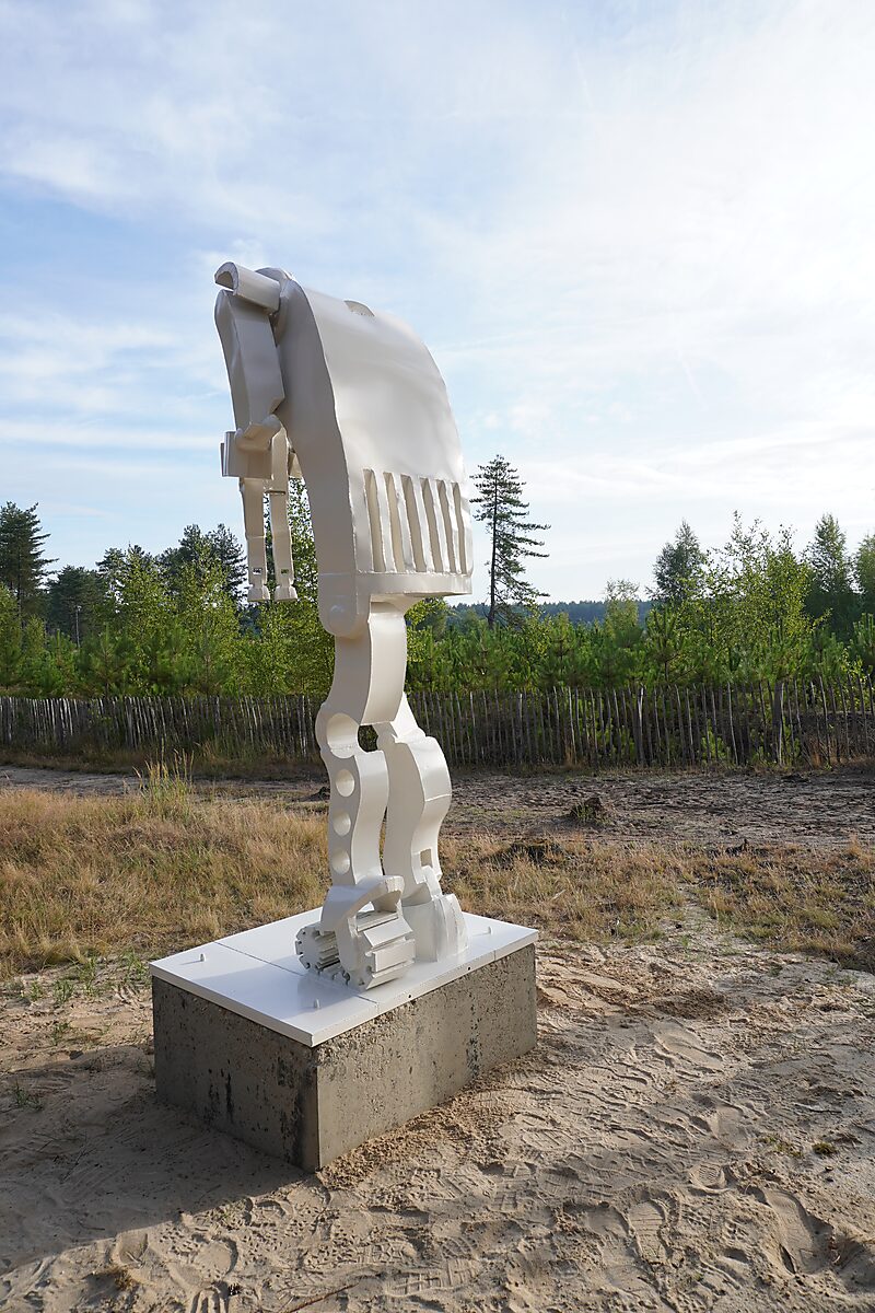 Saturnus — detailaanzicht van de achterzijde van de witte sculptuur, met afgeronde rugvorm en ritmisch verdeelde openingen, geplaatst op een betonnen sokkel in het natuurlijke landschap.