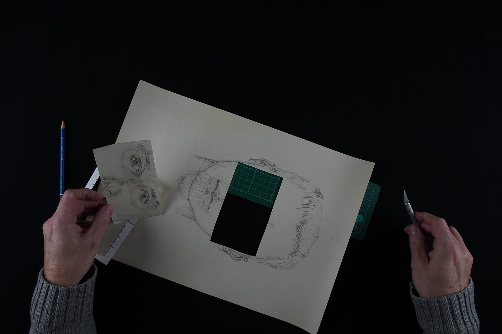 Naming–Value Butterflies — process drawing: study self-portrait 1 PHIKO (1993) — the drawn face lies tilted on the table with a rectangular opening cut over the eyes; one hand holds a small fragment with the eyes.