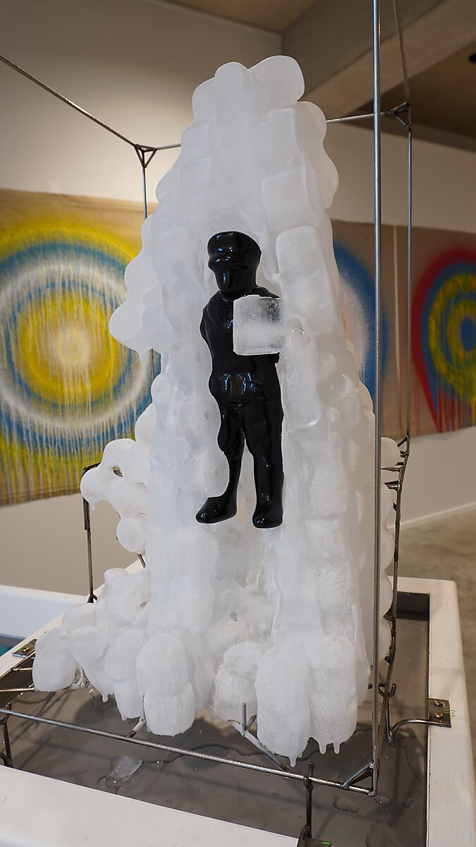 De ijskoude man — op de tentoonstelling Transformatiestudio nr.1: warm of koud bij CC De Adelberg in Lommel: een zwarte figuur is ingesloten in een groeiende massa ijsblokken binnen een metalen frame.