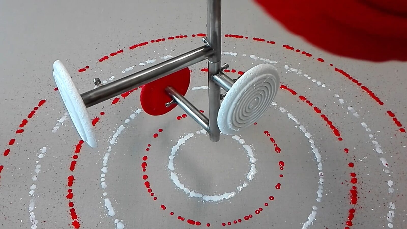 Smeltende doelen nr. 3 — videostill van het druppelproces waarbij de roterende doelen een patroon van rode en witte cirkels op het doek vormen.