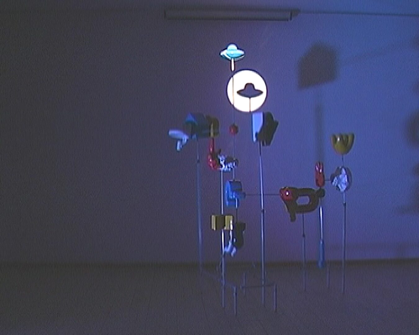 Kies en verander, Ongeïdentificeerde Arcade — foto’s van de installatie en opstelling: hangende vormen in een verduisterde ruimte, met een ronde lichtprojectie en een ufo-vorm centraal.
