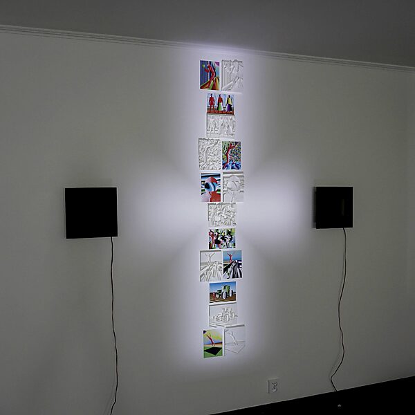 Racer Malevich — studio installation in a cross formation: on a white wall a vertical sequence of prints and white 3D reliefs of Racer Malevich forms a column, flanked by two black square frames with LED light.