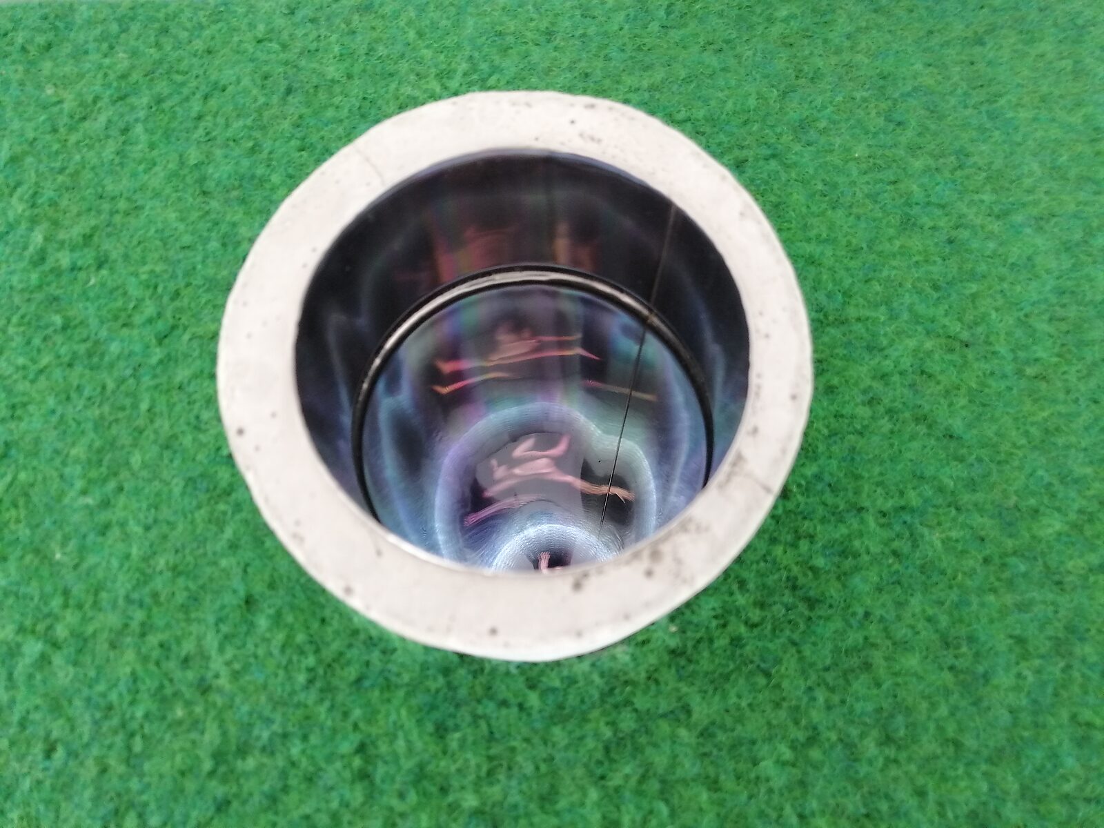 Put van fluïditeiten — bovenaanzicht in de ronde opening waarbij een reflecterende cilindrische schacht zichtbaar wordt in het interieur van de sculptuur.
