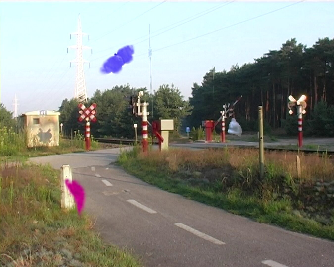 Beweging en verstilling — On the Origin of Butterflies — videostill waarin enkele gekleurde vlindervormen door het beeld zweven boven de weg en de spoorwegovergang.