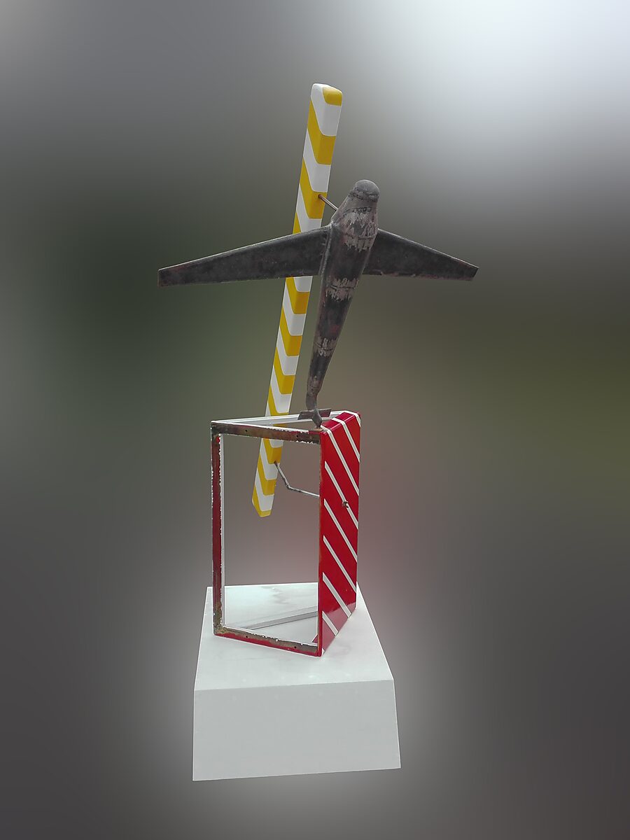 Gelovige vliegtuigen — achteraanzicht van een metalen vliegtuigsculptuur bevestigd aan een minimalistisch frame met diagonale kleurvlakken, geplaatst op een witte sokkel tegen een neutrale achtergrond.