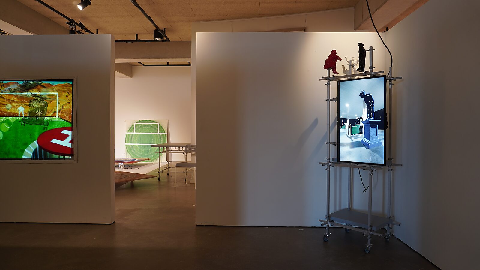 The Bending Monument — exhibition Transformation Studio No.1: Warm or Cold, CC De Adelberg Lommel: a monitor on a wheeled metal frame shows the 3D animation of the Bending Monument within an exhibition space containing several installations and paintings.
