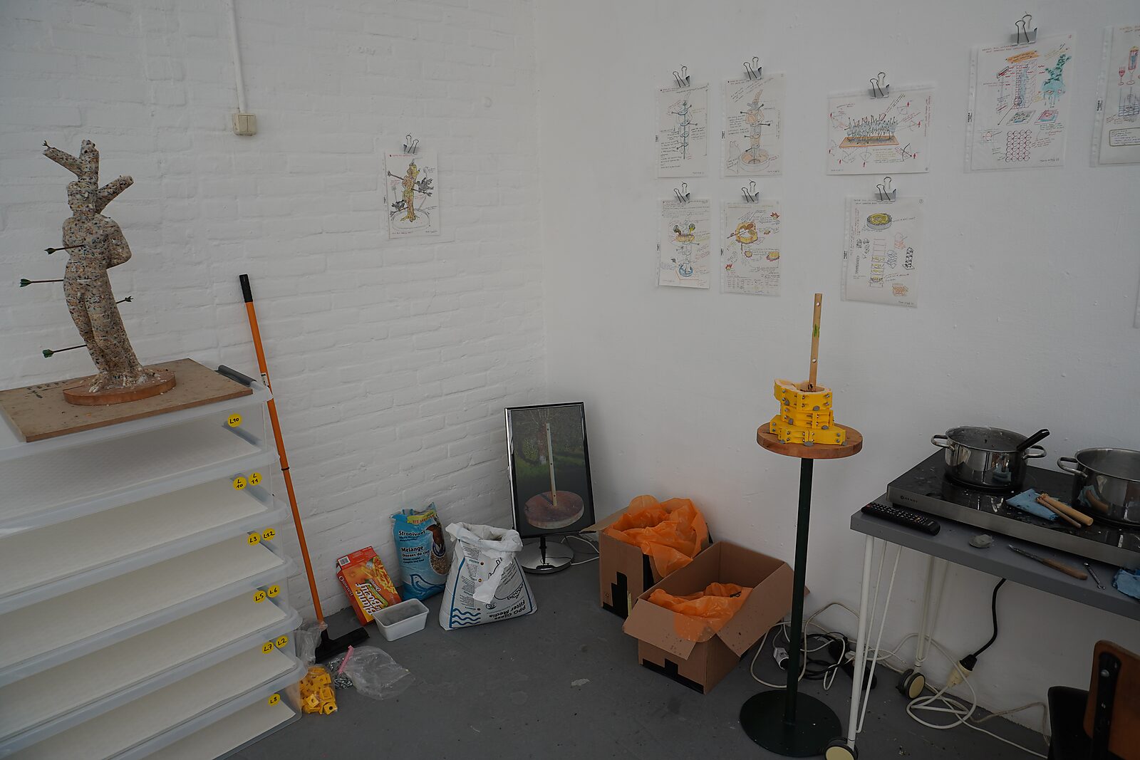 The Great Escape of Saint Sebastian — preparation space with sketches and materials for the project: test sculpture of Saint Sebastian, molds, bags of materials, and a hot plate with pots used to melt beef fat.