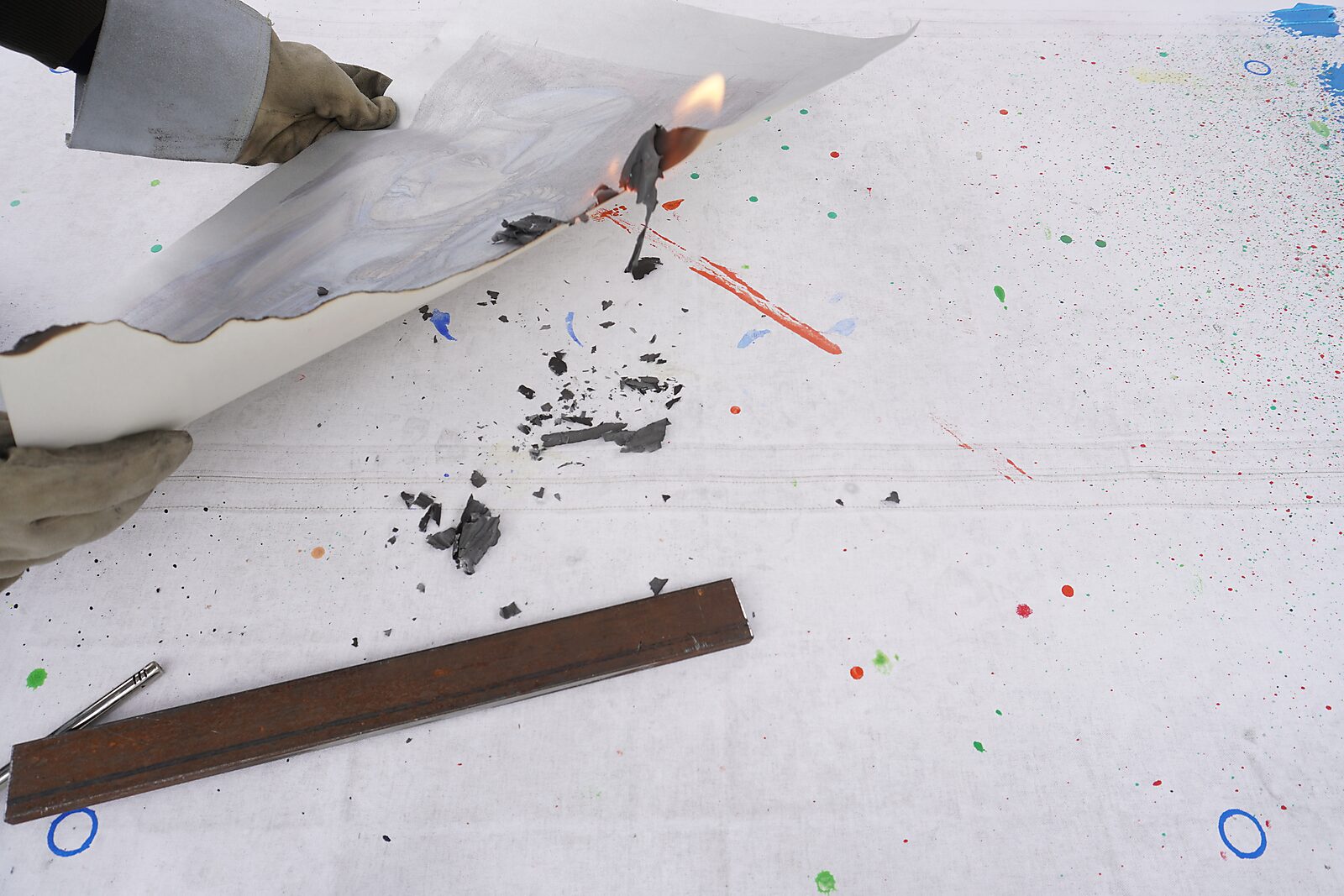 Naming–Value Butterflies — process drawing: Robotman (1995) — a gloved hand holds the paper while the edge starts to burn; charred fragments and ash scatter across the table.