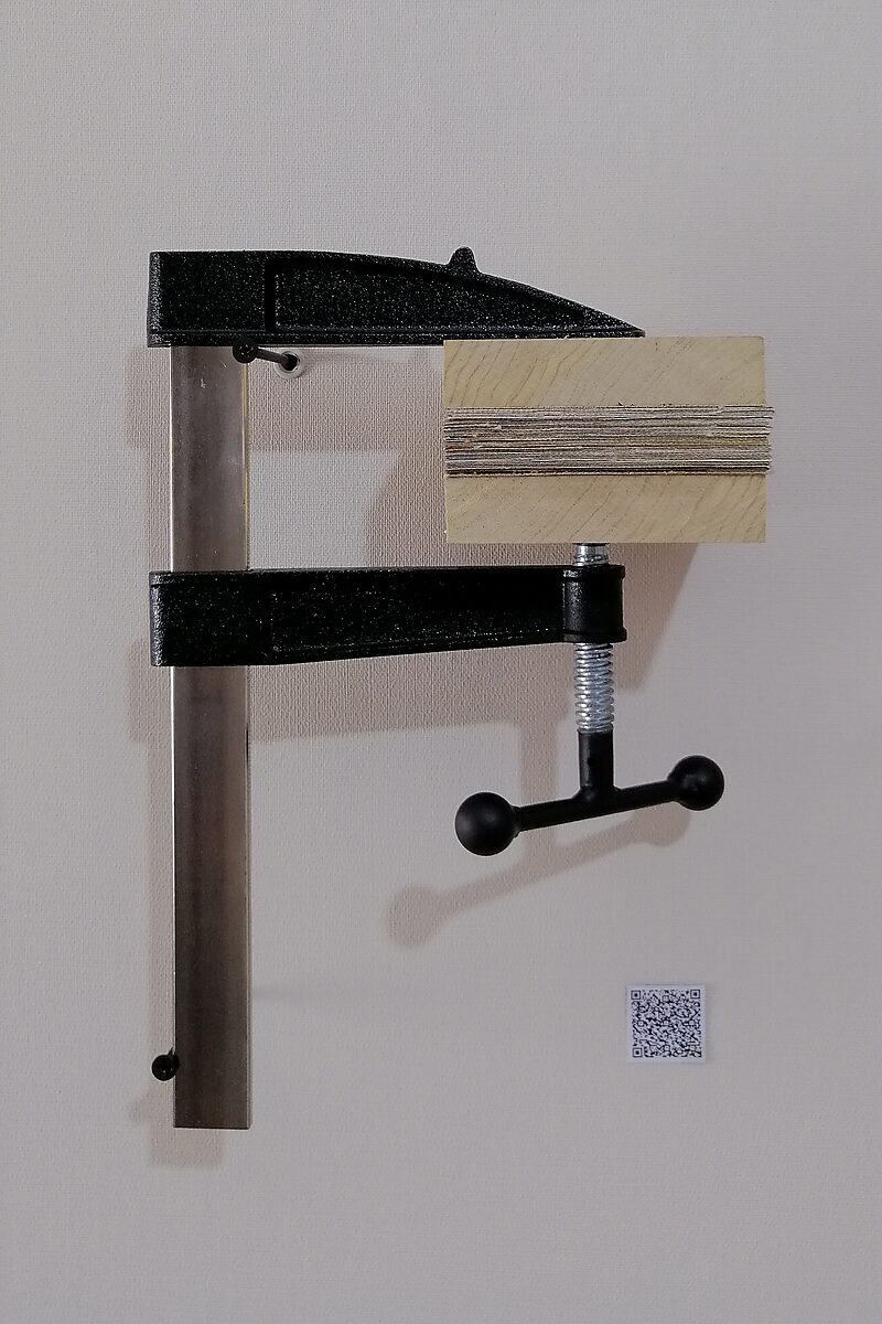 Paintings.zip — a wall-mounted clamp presses a stack of cut painting fragments together between two wooden plates; the object functions as a physical analogy of digital compression.