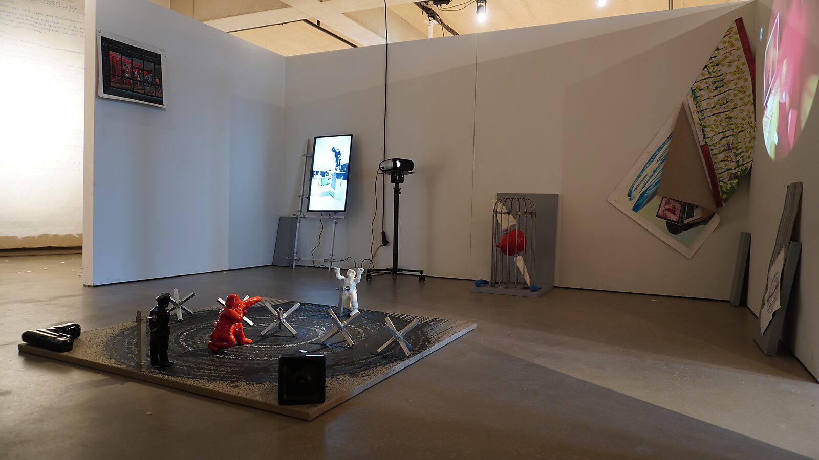 Het Buigend Monument — tentoonstelling Transformatiestudio nr.1: warm of koud, CC De Adelberg Lommel: overzicht van een tentoonstellingsruimte met een vloerinstallatie met kleine figuren en metalen obstakels, terwijl op een monitor de animatie van het Bui