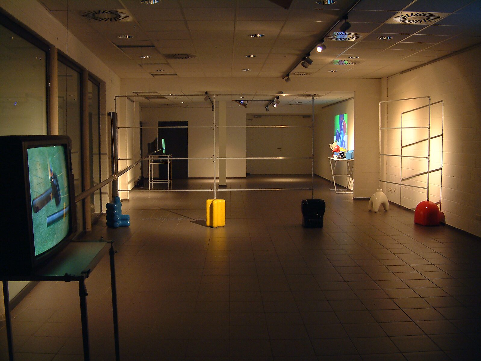 'Kies en verander project’: Tentoonstellingszicht met meerdere metalen buisconstructies in de ruimte; televisiemonitor links en videoprojectie achteraan, CC De Kollebloem, Puurs, 2008.