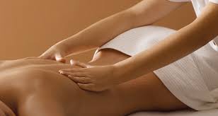 Une femme est allongée sur une table de massage avec une serviette recouvrant le bas de son corps. Une personne lui masse le dos
