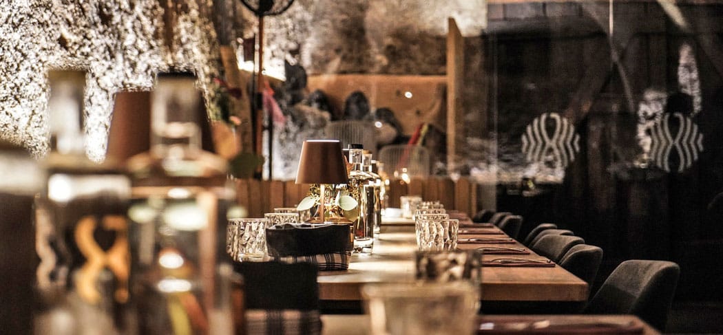 Gemütlich gedeckter Tisch im Spuntloch Kaltern mit warmem Licht, edlen Gläsern und Felswänden – stimmungsvolles Ambiente in einem schönen Restaurant in Kaltern.