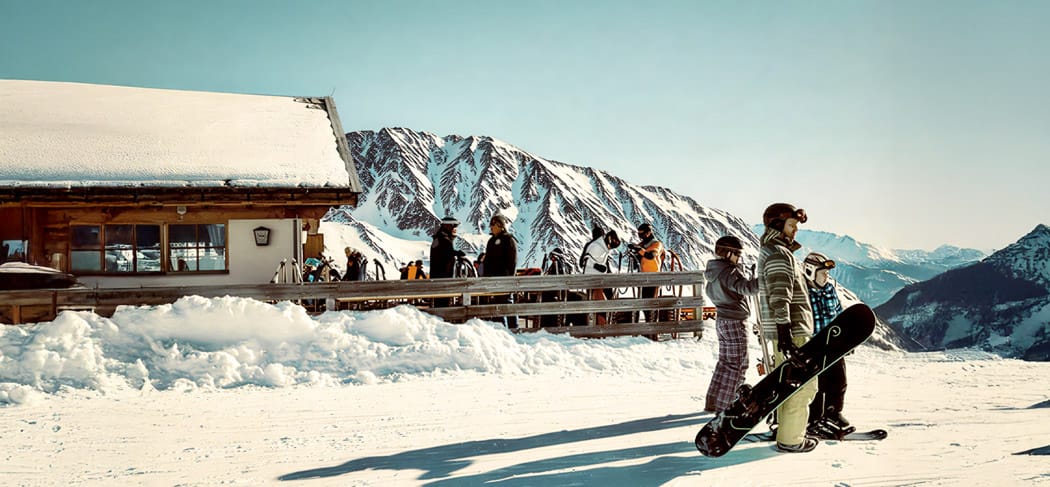 Skifahrer und Snowboarder vor der Lazaunhütte im Schnalstal, sonnige Terrasse im Winter, verschneite Berge und Hochalpen-Panorama oberhalb von Kurzras.