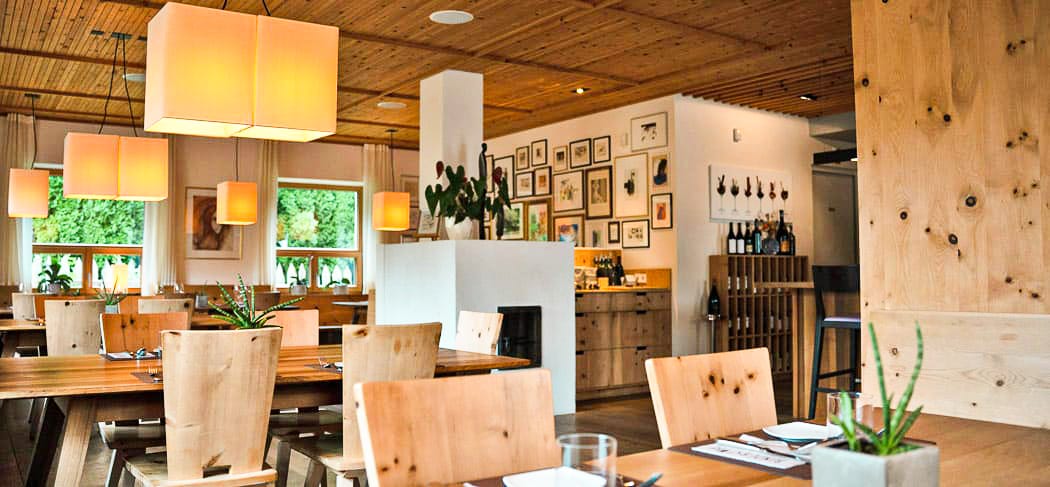 Sala moderna del ristorante Binderstube a Fiè allo Sciliar con arredi in legno, luce calda, tavoli apparecchiati e atmosfera accogliente ed elegante.