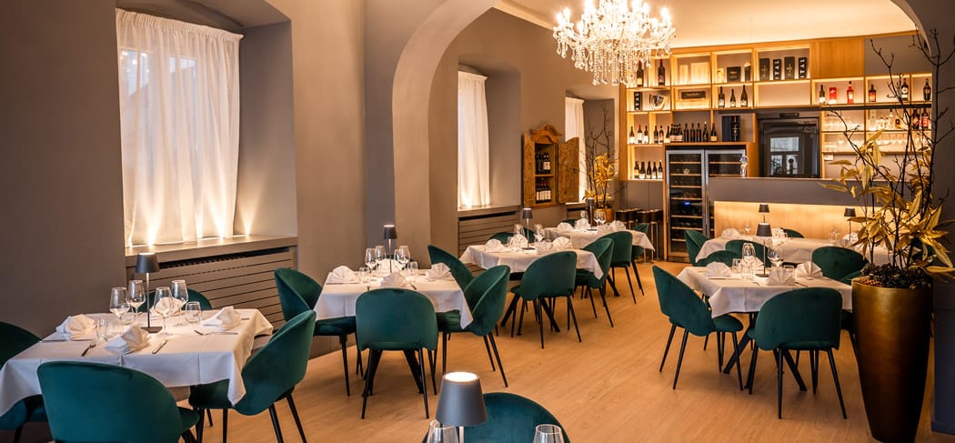 Elegante sala ristorante al Primo Piano a Bolzano: tavoli apparecchiati con stile, raffinate sedie in velluto, lampadari a braccio e cantinetta in un esclusivo locale per eventi nel cuore del centro storico.