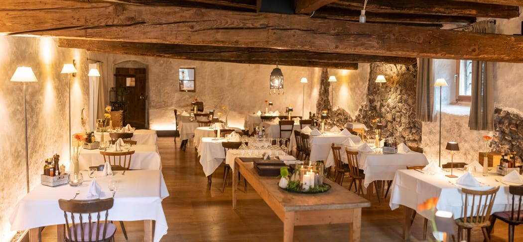 Sala ristorante arredata con stile al Rössl Bianco di Merano con soffitto con travi in legno, pareti in pietra, candele e luci calde: un ambiente elegante e accogliente dove godersi ogni momento.