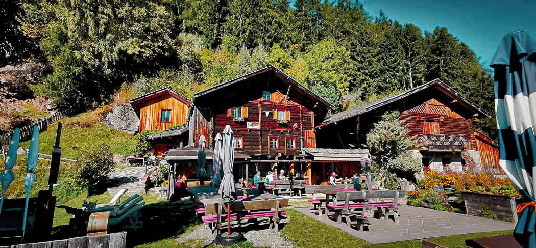 Gemütliche Jausenstation Naserhof im Kalmtal bei St. Martin in Passeier mit sonniger Terrasse, blühendem Garten und traditionellem Holzbau vor beeindruckender Bergkulisse.