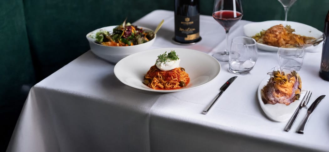 Genuss im Restaurant Ban Max in Truden: stilvoll gedeckter Tisch mit Pasta, Salat, Fleischgericht und Wein – italienische Küche in Südtirol.