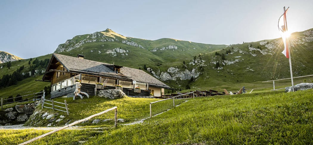 La Malga Gampen a Funes all'alba, circondata da prati verdi e montagne: meta escursionistica molto apprezzata con rifugio e vista sulle Dolomiti.