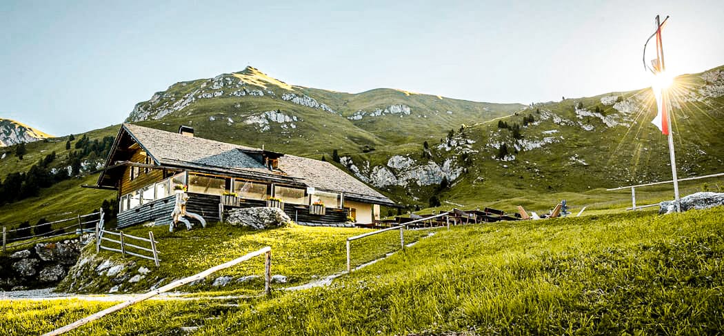 La Malga Gampen a Funes all'alba, circondata da prati verdi e montagne: meta escursionistica molto apprezzata con rifugio e vista sulle Dolomiti.