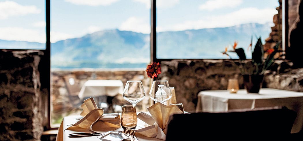 Gedeckter Tisch im Restaurant Castel Haselburg in Bozen mit Blick auf die Berge; elegantes Ambiente eines Gourmetlokals in Südtirol.