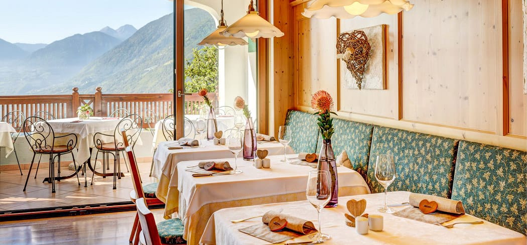 Helle Tiroler Stube im Restaurant Sonne Dorf Tirol mit Panoramablick auf Meran, stilvoll gedeckte Tische, Holzinterieur und gemütliche Atmosphäre