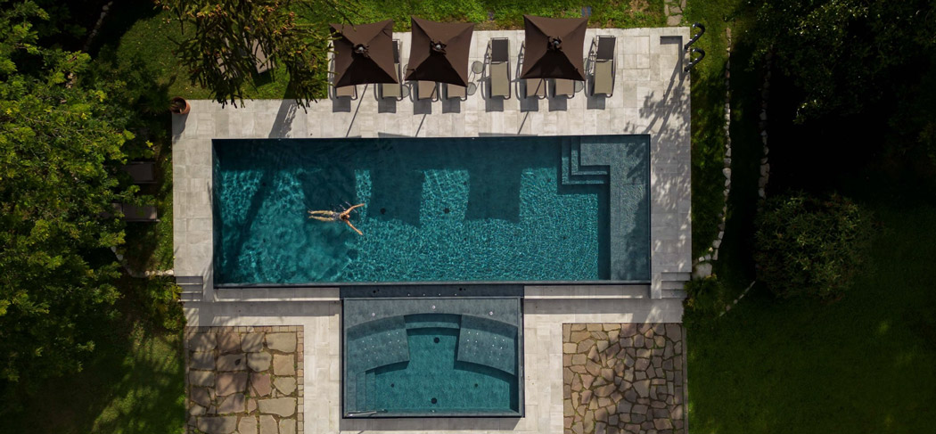 Veduta dall'alto della piscina esterna dell'Hotel Castel Rundegg a Merano, con lettini e ombrelloni nell'ampio giardino dell'hotel: il luogo perfetto per rilassarsi completamente.