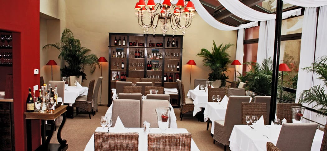 Eleganter Innenbereich des Bistro Seven in Meran mit stilvoll gedeckten Tischen, roten Kronleuchtern und mediterranem Ambiente unter den historischen Lauben.