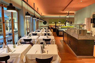 Elegante sala del Pizzeria Ristorante Gaston a Merano con tavoli apparecchiati, illuminazione moderna e atmosfera mediterranea sotto i Portici.