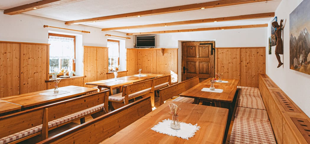 Traditioneller Gastraum mit Holzvertäfelung, langen Holzbänken mit gepolsterten Sitzflächen, Blumenvasen auf den Tischen, Holzdecke und rustikalem Charme im Gasthof Helener Pichl im Ultental.