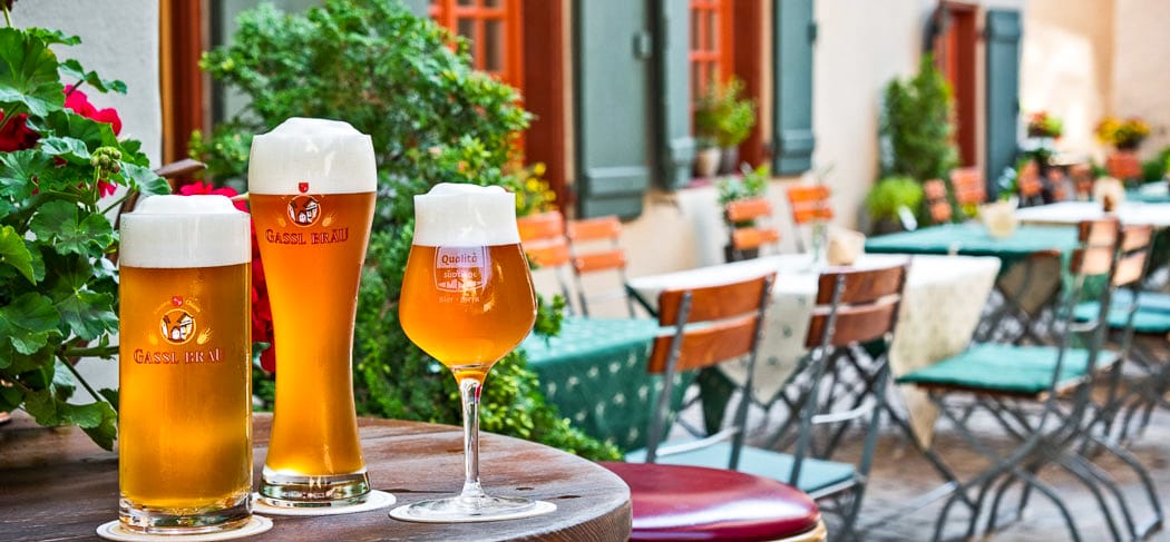 Drei hausgebraute Biere des Restaurants Gassl Bräu in Klausen auf einem Holztisch im gemütlichen Brauereigarten – Genuss in der historischen Altstadt.