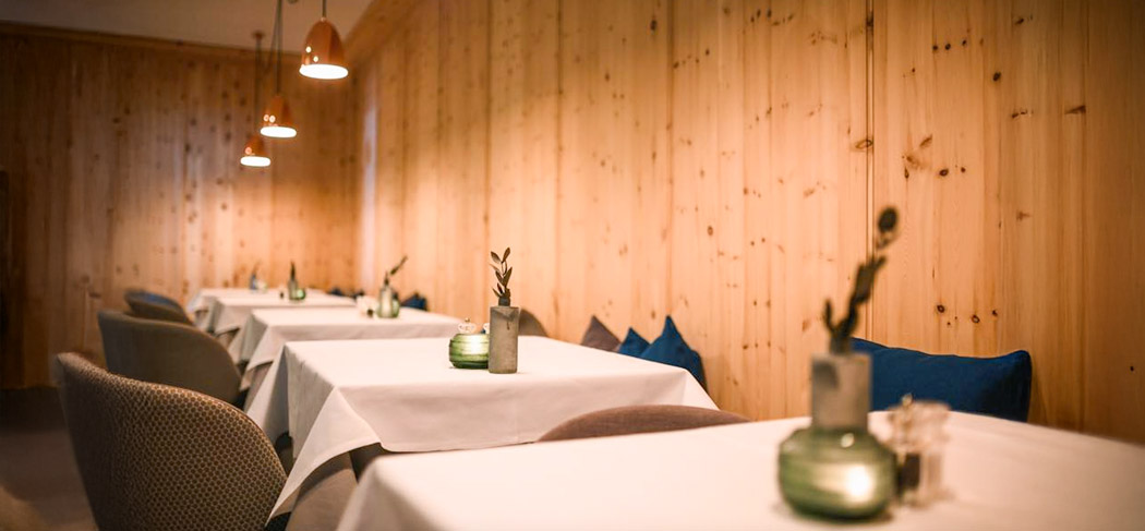 Accogliente sala ristorante con rivestimenti in legno, tavoli apparecchiati con tovaglie bianche e luci calde all'Adlernest Bistro a Nostra Signora in Val Senales.