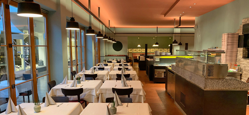 L'elegante sala del Ristorante-Pizzeria Gaston a Merano, con tavoli apparecchiati, un moderno sistema di illuminazione e un'atmosfera mediterranea sotto i pergolati.