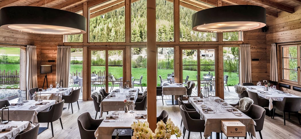 Restaurant Eggile im Chaletdorf Valsegg in Vals: stilvoller Speisesaal mit Panoramafenstern, modernem Alpendesign und Blick auf die Wälder des Valler Tals in Südtirol.