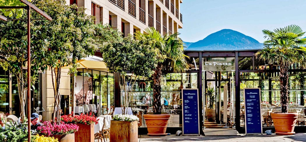 Terrazza suggestiva del ristorante & bistrot La Piazza a Merano con palme e vista sulle montagne dell'Alto Adige