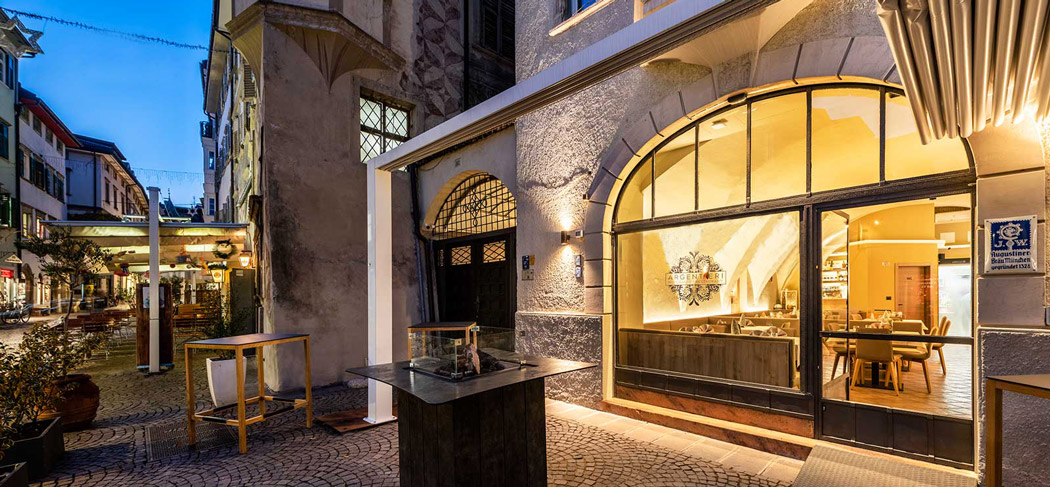 Außenansicht des Restaurants Argentieri in der Bozner Altstadt mit stilvoll gedeckter Terrasse, Sonnenschirmen und Menütafel auf Kopfsteinpflaster.