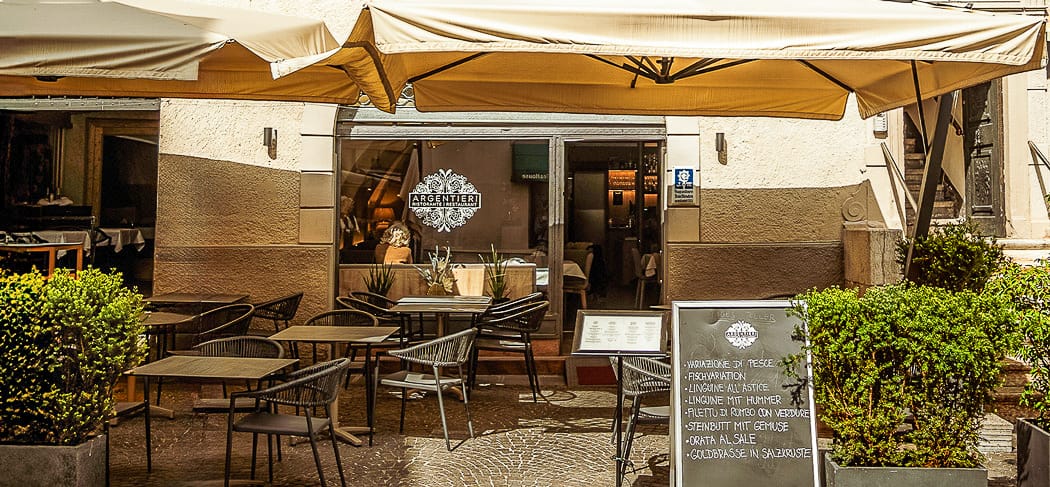 Außenbereich des Restaurant Argentieri in Bozen mit Sonnenschirmen, Terrasse, gedeckten Tischen und Menütafel vor dem Fischrestaurant in der Altstadt.