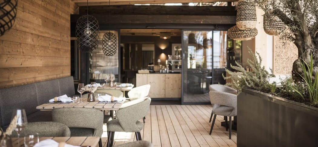 Stilvolle Panoramaterrasse im Restaurant Presulis in Völs am Schlern mit Holzboden, Designlampen, gedeckten Tischen und Blick ins moderne Interieur.