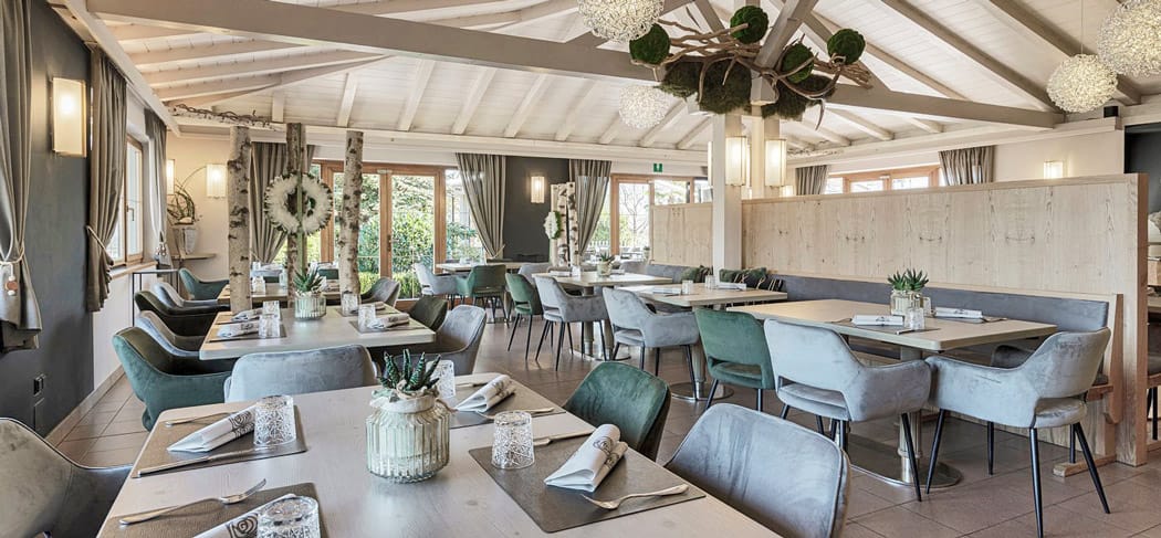 Restaurant Wiesenheim in Eppan: heller Speisesaal mit modernem Alpenflair, stilvollen Deko-Details, gemütlichen Stühlen und großen Fenstern mit Gartenblick.